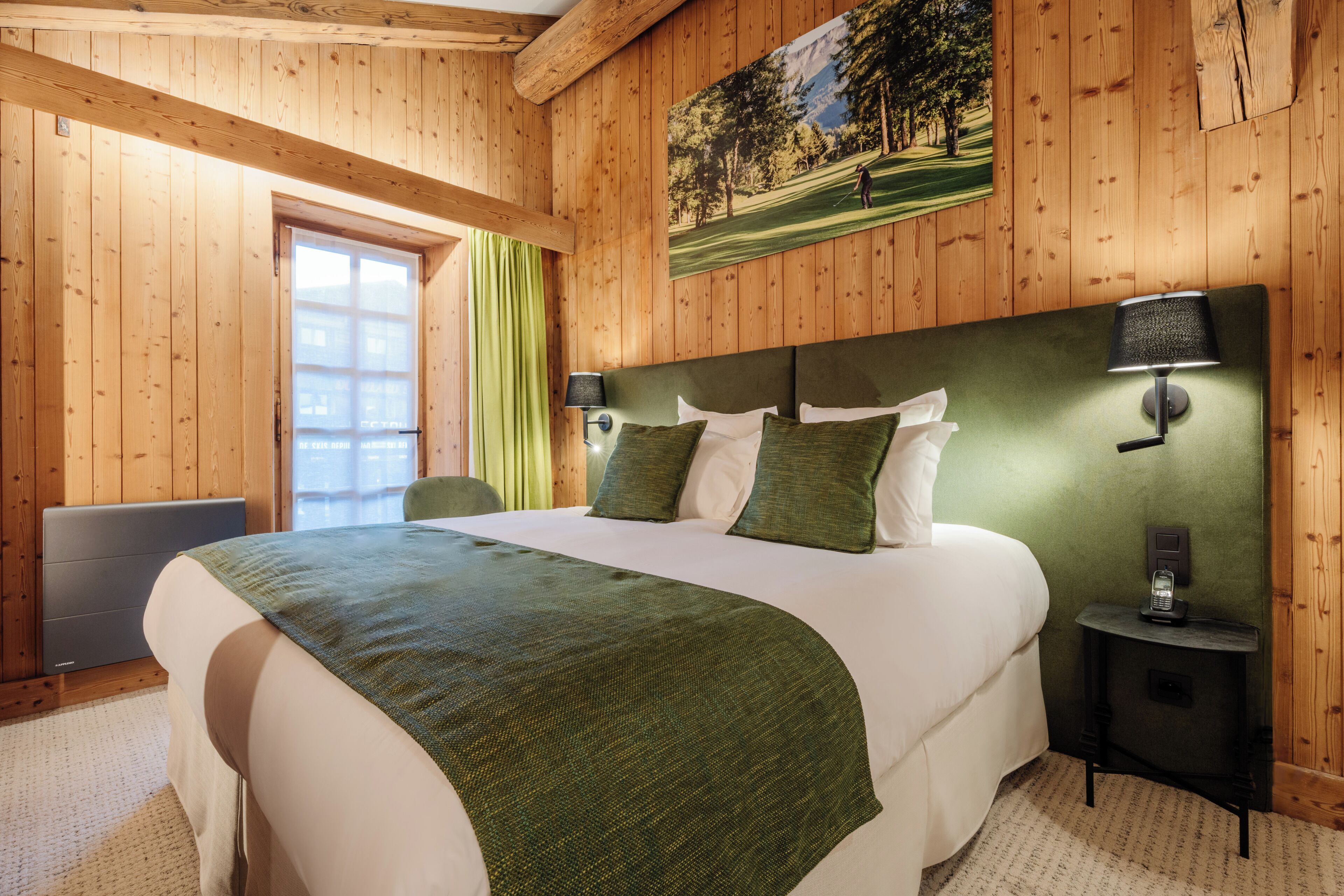 Une chambre à coucher aux murs lambrissés, avec un grand lit, une literie verte, une tête de lit dotée d’une lampe et un tableau représentant un terrain de golf.