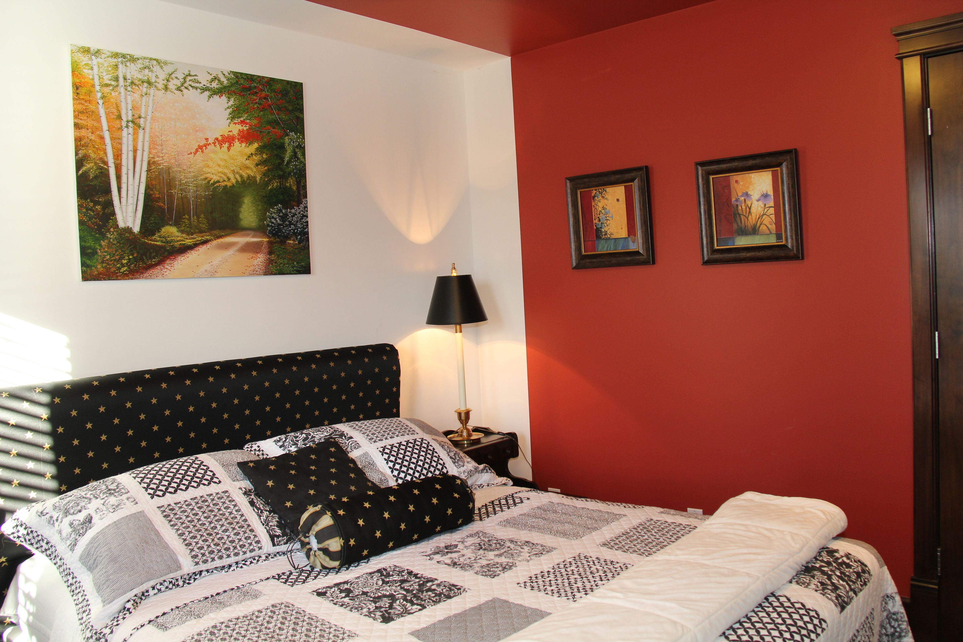 Un dormitorio con una cama, una mesita de noche, una lámpara y dos cuadros en la pared.