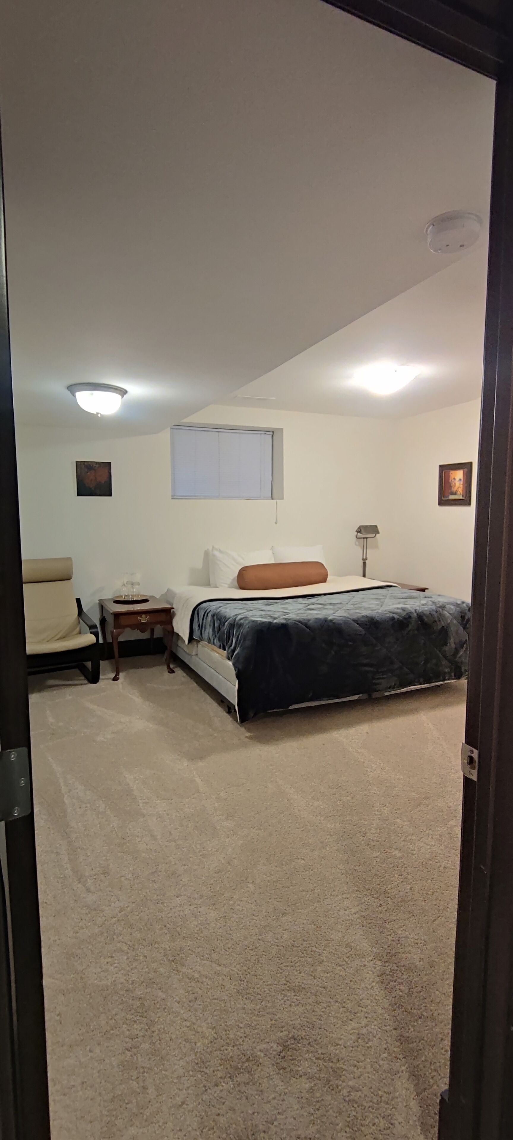 Une chambre à coucher comprenant un lit, une chaise, une table de chevet, une lampe et un luminaire au plafond.