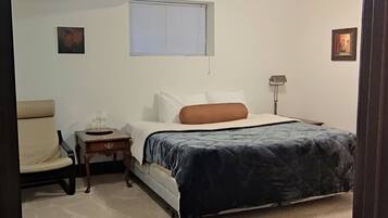 Une chambre à coucher comprenant un lit, une chaise, une table de chevet, une lampe et un luminaire au plafond.