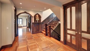A spacious hallway with wooden flooring, a grand staircase, and a large wooden door with glass panels. - Westmount River Inn (Calgary)