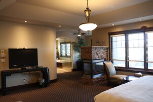 A hotel room with a television, a fireplace, a large window, and a ceiling fan.