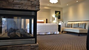 A hotel room with a stone fireplace, a bed with white bedding, a sofa, and a painting on the wall. - Westmount River Inn (Calgary)
