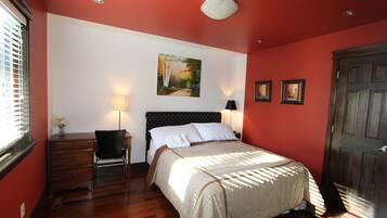 A bedroom with a bed, a desk, and a chair. There is a painting on the wall and a door to the right.