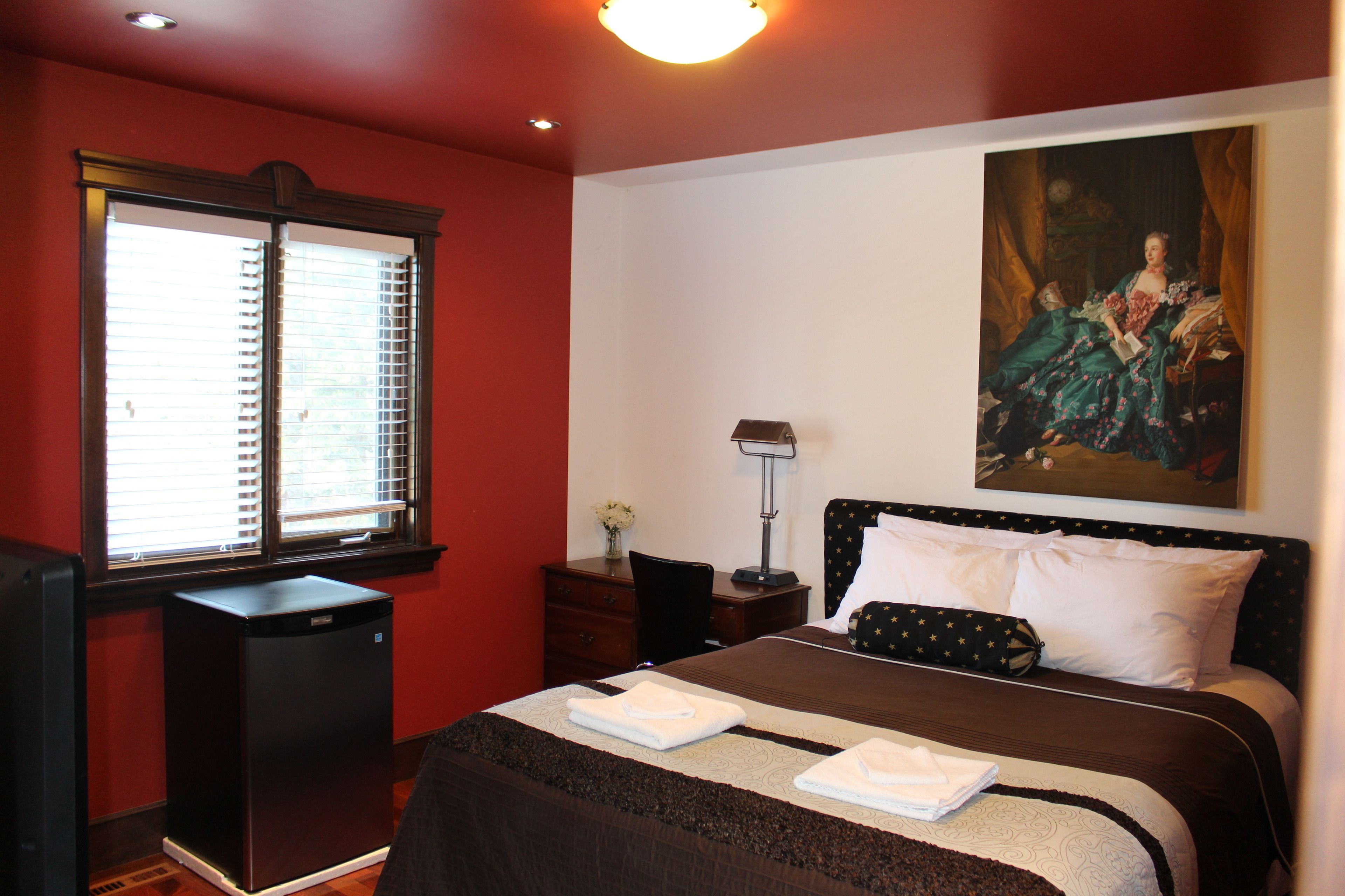 Une chambre d’hôtel avec un lit, un bureau, une chaise, une lampe et un tableau au mur.