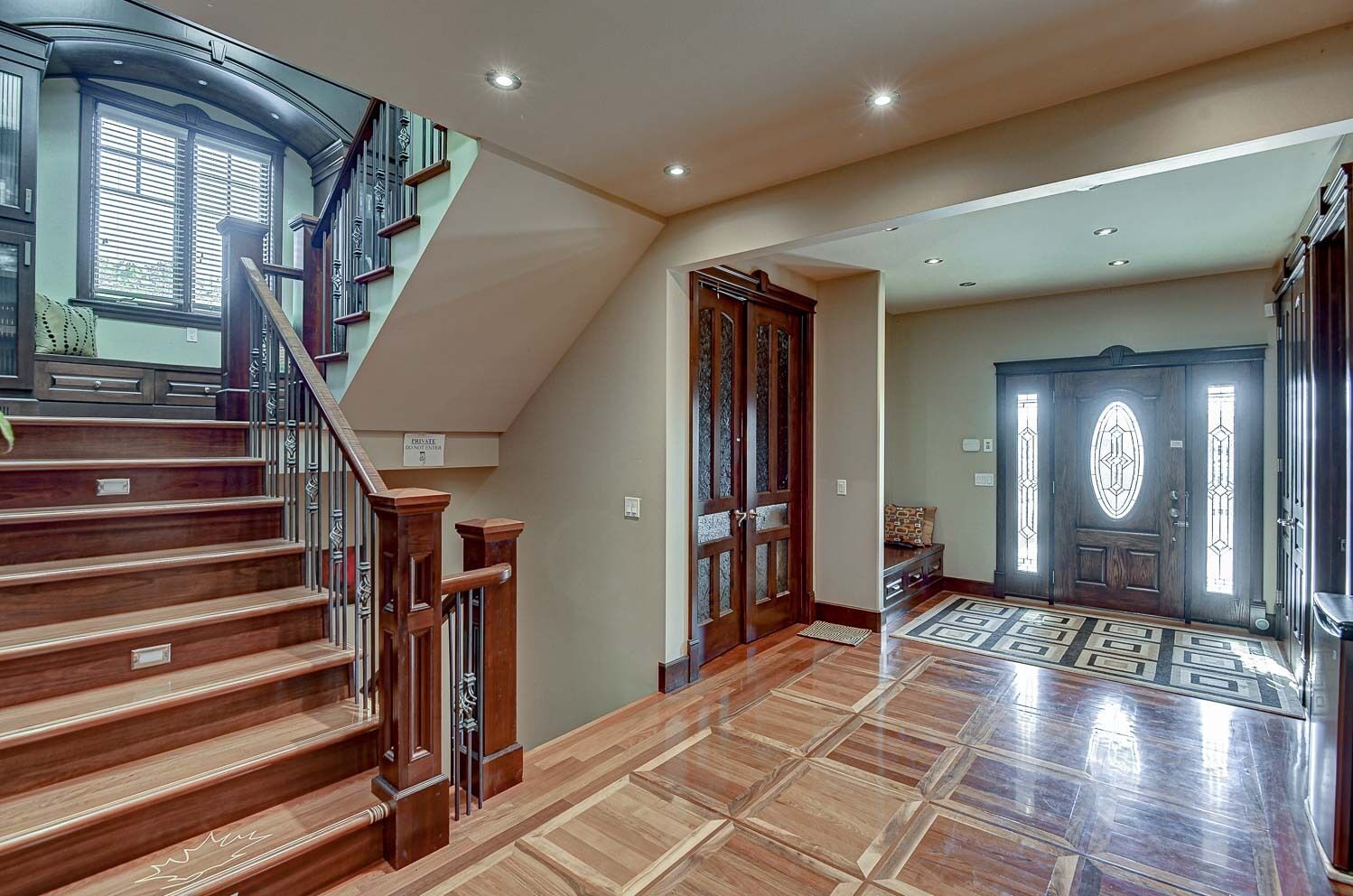 A spacious foyer with a grand staircase, a large wooden door, and a patterned rug.