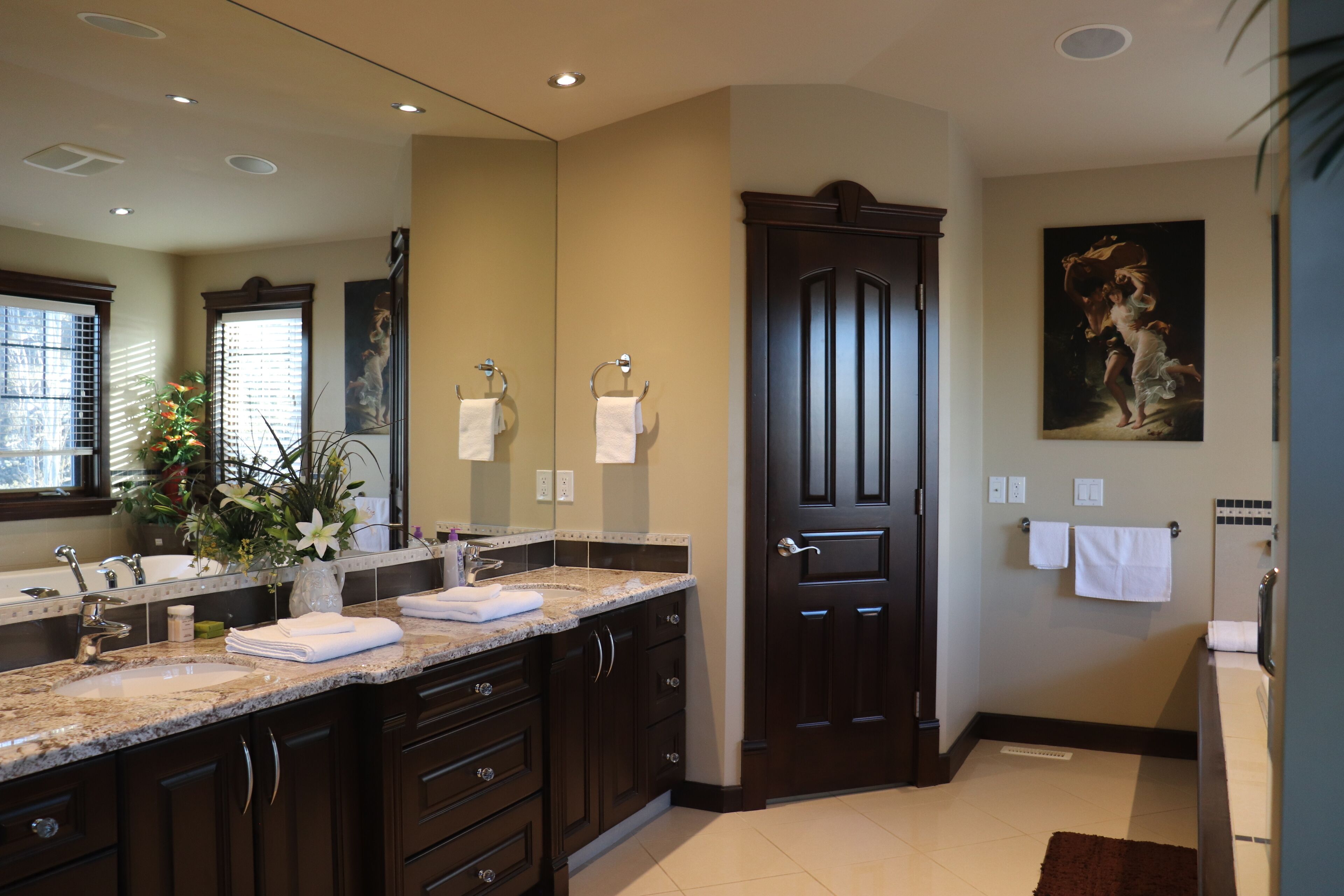 A modern bathroom with dark wood cabinetry, a large mirror, and a painting on the wall.