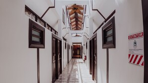 A long, narrow hallway with a patterned floor, wooden doors on both sides, and a ceiling fan. - Dunn Inn (San José)