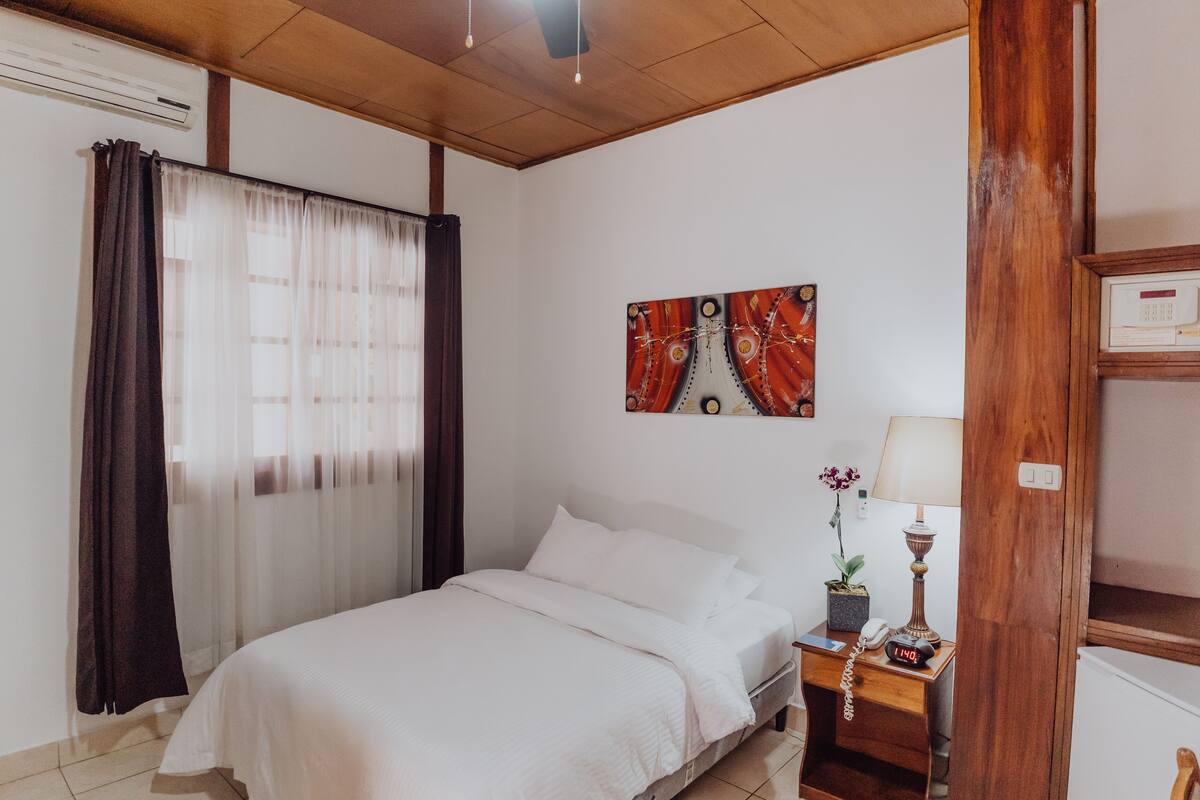 Un dormitorio con cama, mesita de noche con lámpara, un reloj de pared y un calendario.