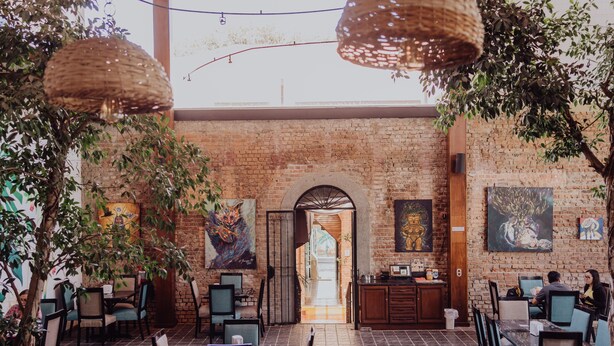An indoor dining area with brick walls, hanging wicker lamps, and artwork on the walls. - Dunn Inn (San José)