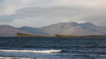 A coastal landscape with mountains in the background and waves approaching the shore.