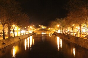 A nighttime view of a canal with a stone bridge, trees lining the banks, and streetlights reflecting on the water. - Brooklodge B&B (Westport)