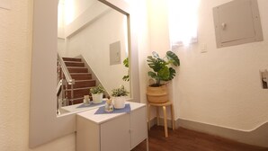 Casa de banho com toucador branco, espelho grande, planta em vaso e banquinho de madeira.