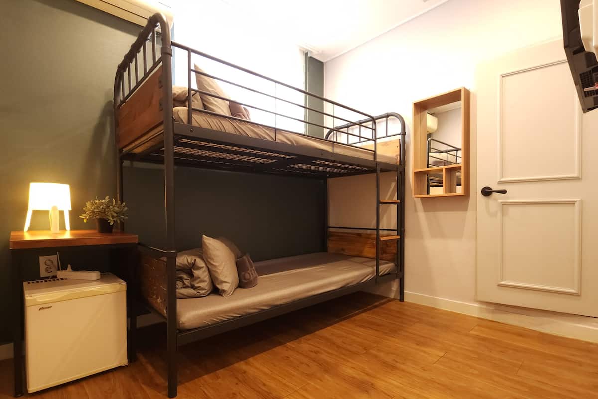 A bunk bed with a desk and a small fridge, a door, and a shelf with items.