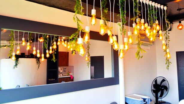 Um interior moderno com luminárias pendentes e plantas, uma área de cozinha visível e um ventilador.