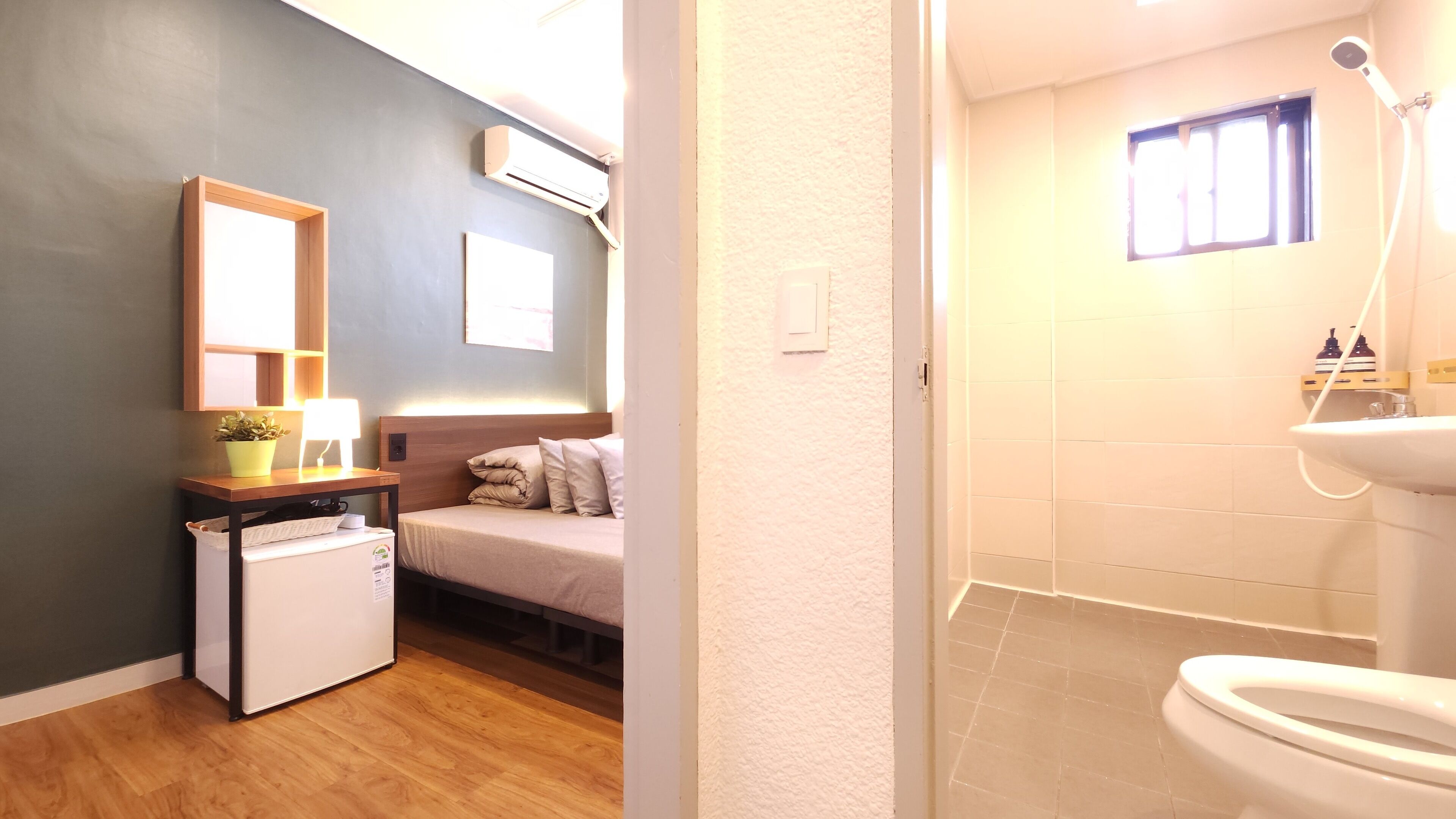 A compact hotel room with a bed, bedside table, lamp, and a small refrigerator.