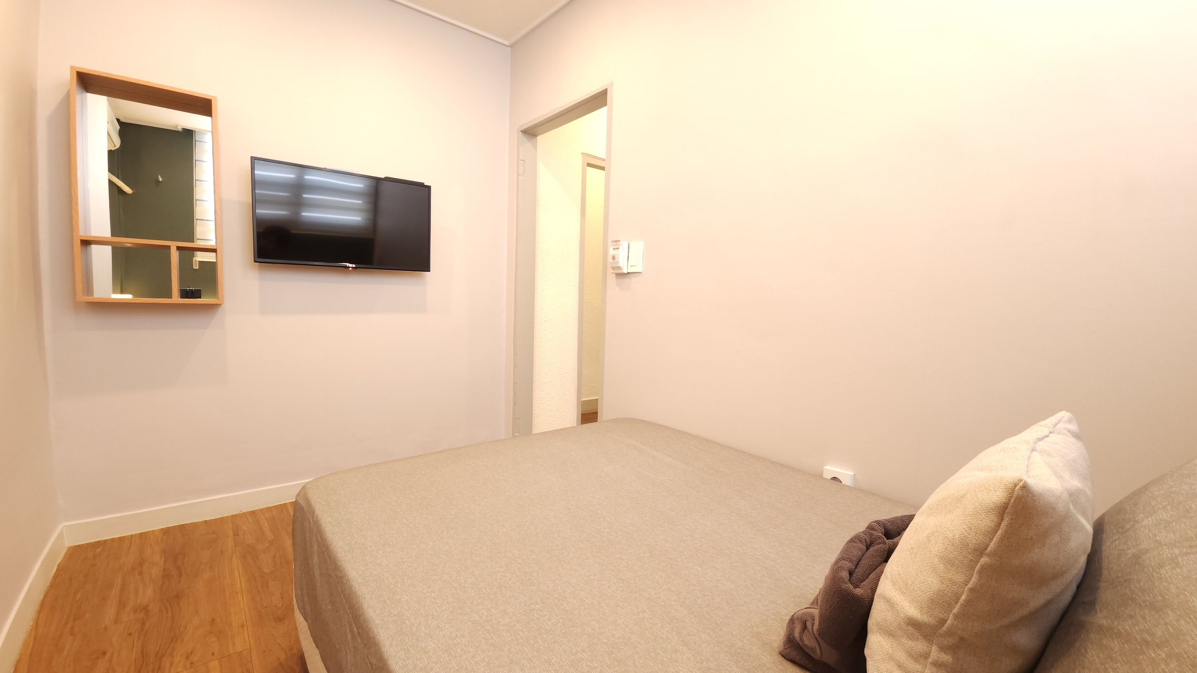 A bedroom with a bed, a television mounted on the wall, and a door leading to another room.