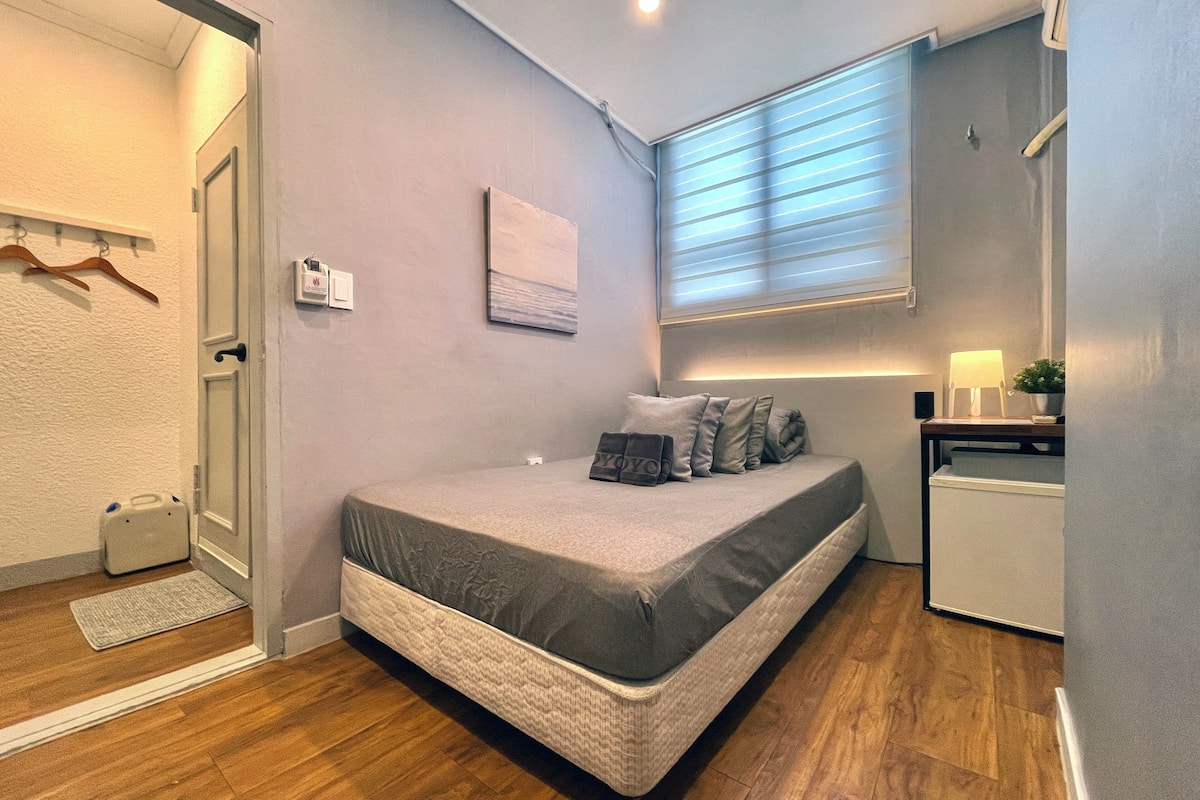 A compact bedroom with a bed, bedside table, lamp, and a small potted plant.