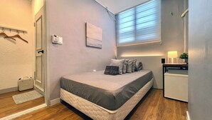 Quarto compacto com cama, mesa de cabeceira, abajur e um pequeno vaso de planta.