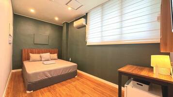 A bedroom with a bed, a desk, a lamp, and a window with blinds.