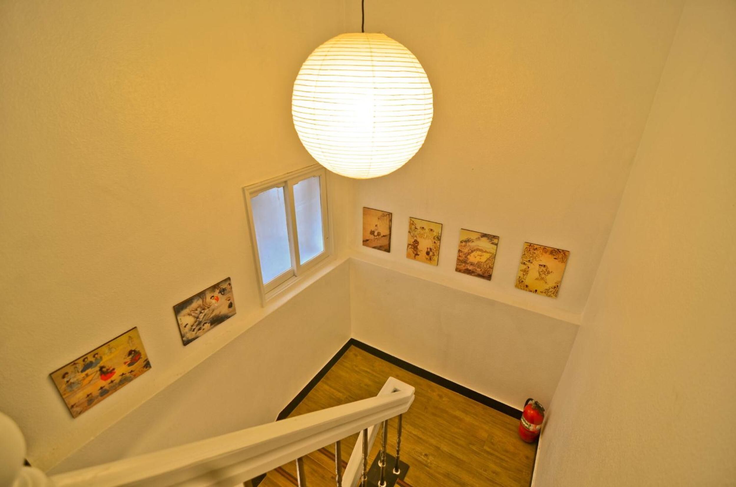 A staircase with a white railing, a hanging paper lantern, and several framed artworks on the walls.