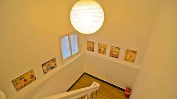 A staircase with a white railing, a hanging paper lantern, and several framed artworks on the walls.