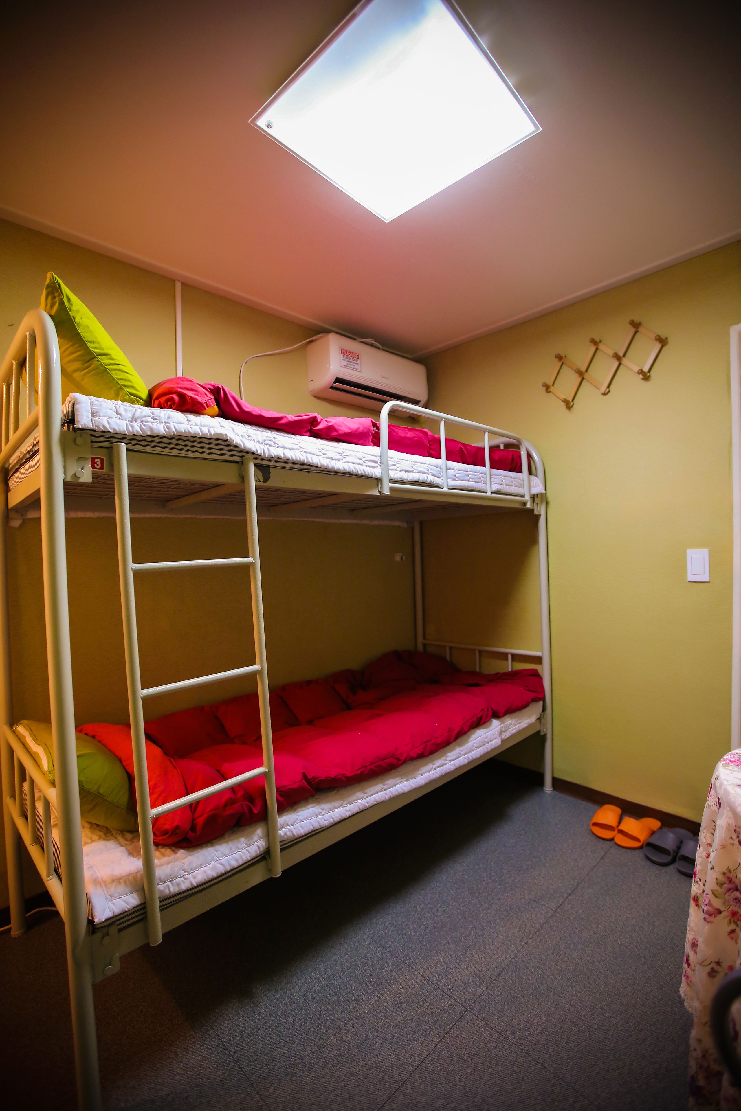 A bunk bed with red bedding, a ladder, and a ceiling light.