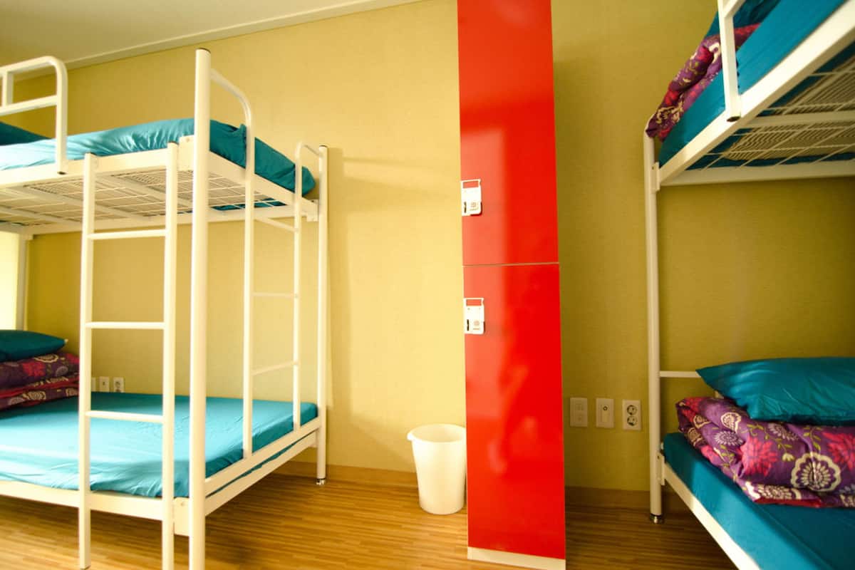A room with bunk beds, a red accent wall, and a white trash bin.