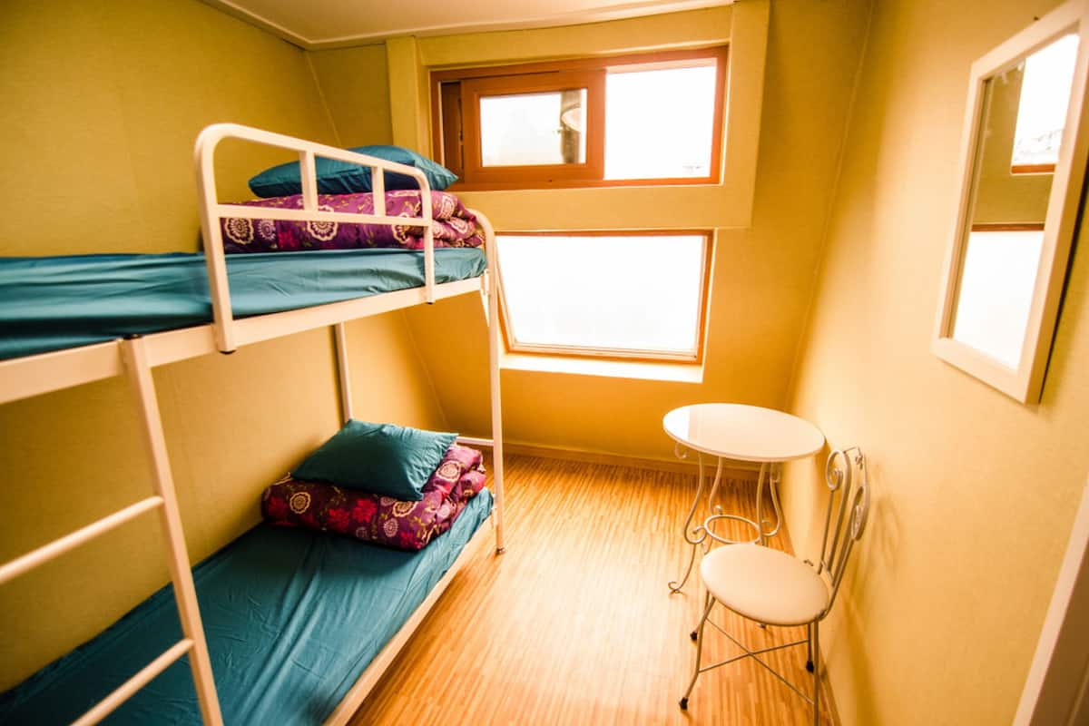 A bunk bed room with a small table and a window.
