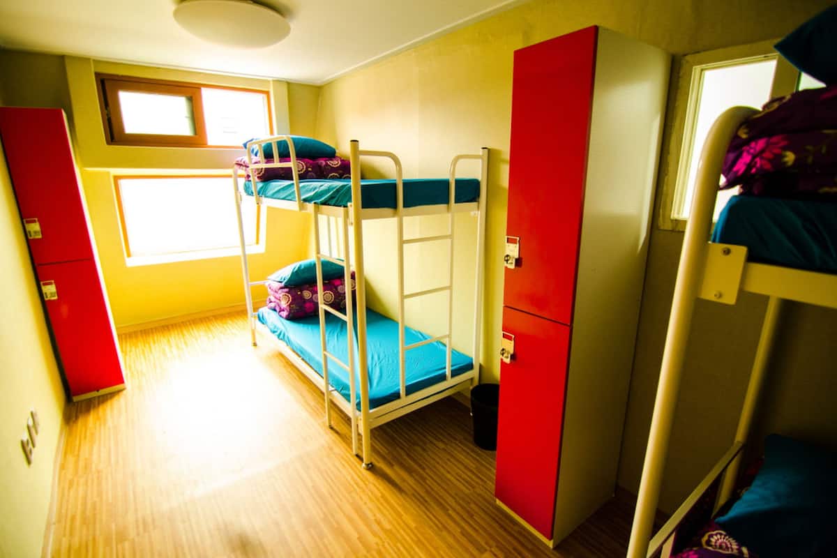 A bunk bed room with a window, a red cabinet, and a wooden floor.