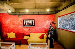Una habitación con una pared cubierta de grafiti rojo, un televisor montado en ella, un sofá amarillo y un árbol de Navidad.