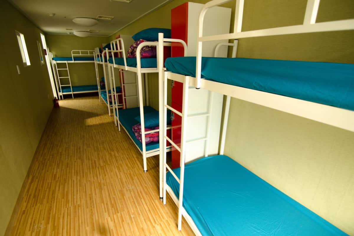A dormitory room with bunk beds, wooden flooring, and a red cabinet.