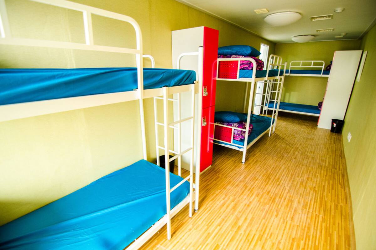 A dormitory room with bunk beds, a red storage unit, and a white wardrobe.