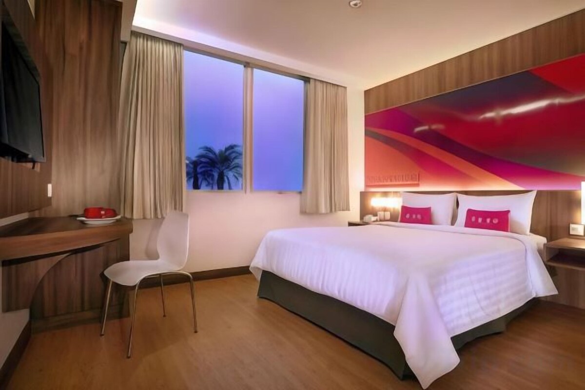 A hotel room with a bed, a desk, a chair, and a window with curtains.