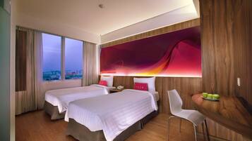 A hotel room with two beds, a desk with a chair, a view of the city, and a large abstract wall art piece.