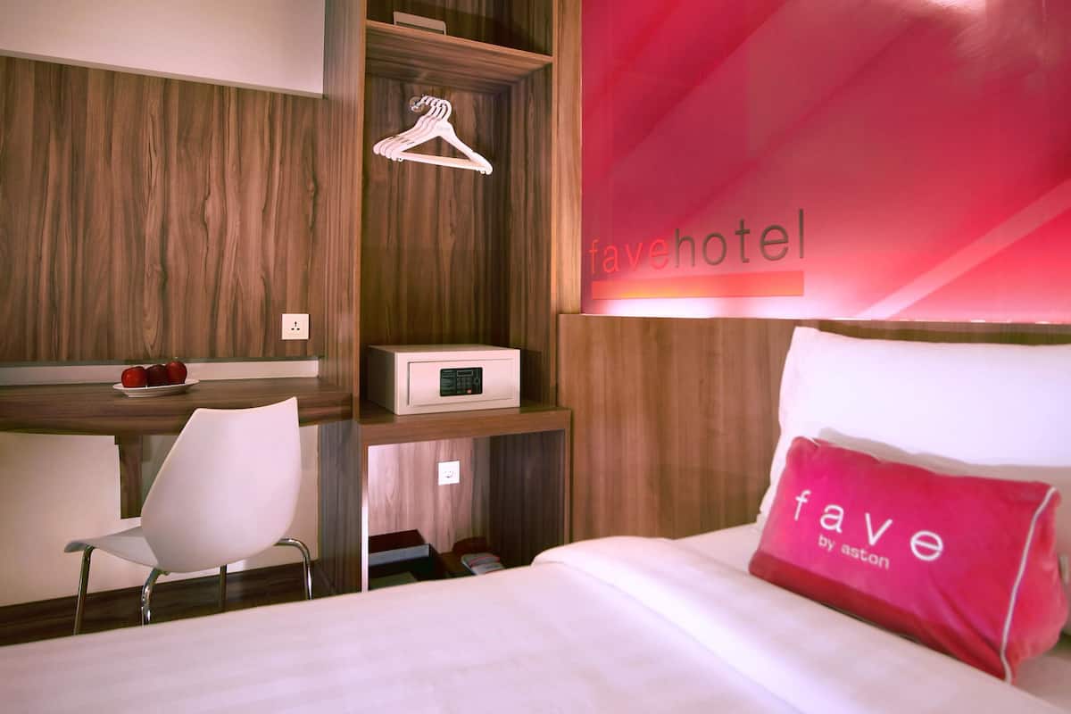 Hotelkamer met een bed, bureau, stoel, garderobe en rode wand met de naam van het hotel.