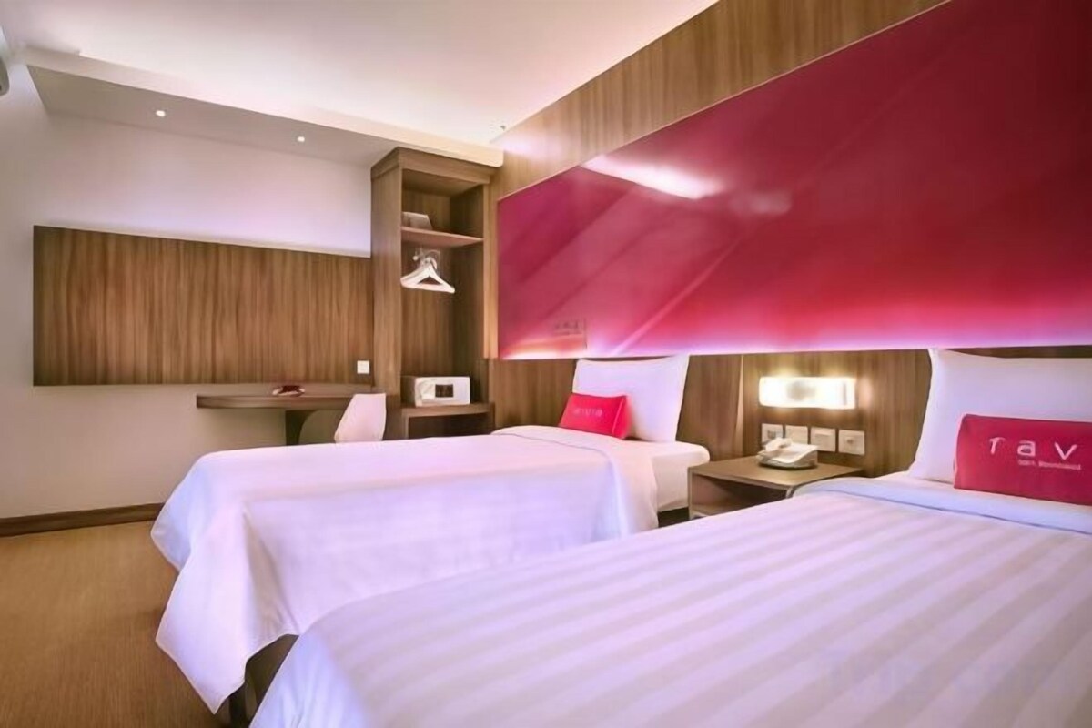 A hotel room with two beds, a desk, a wardrobe, and a red accent wall.