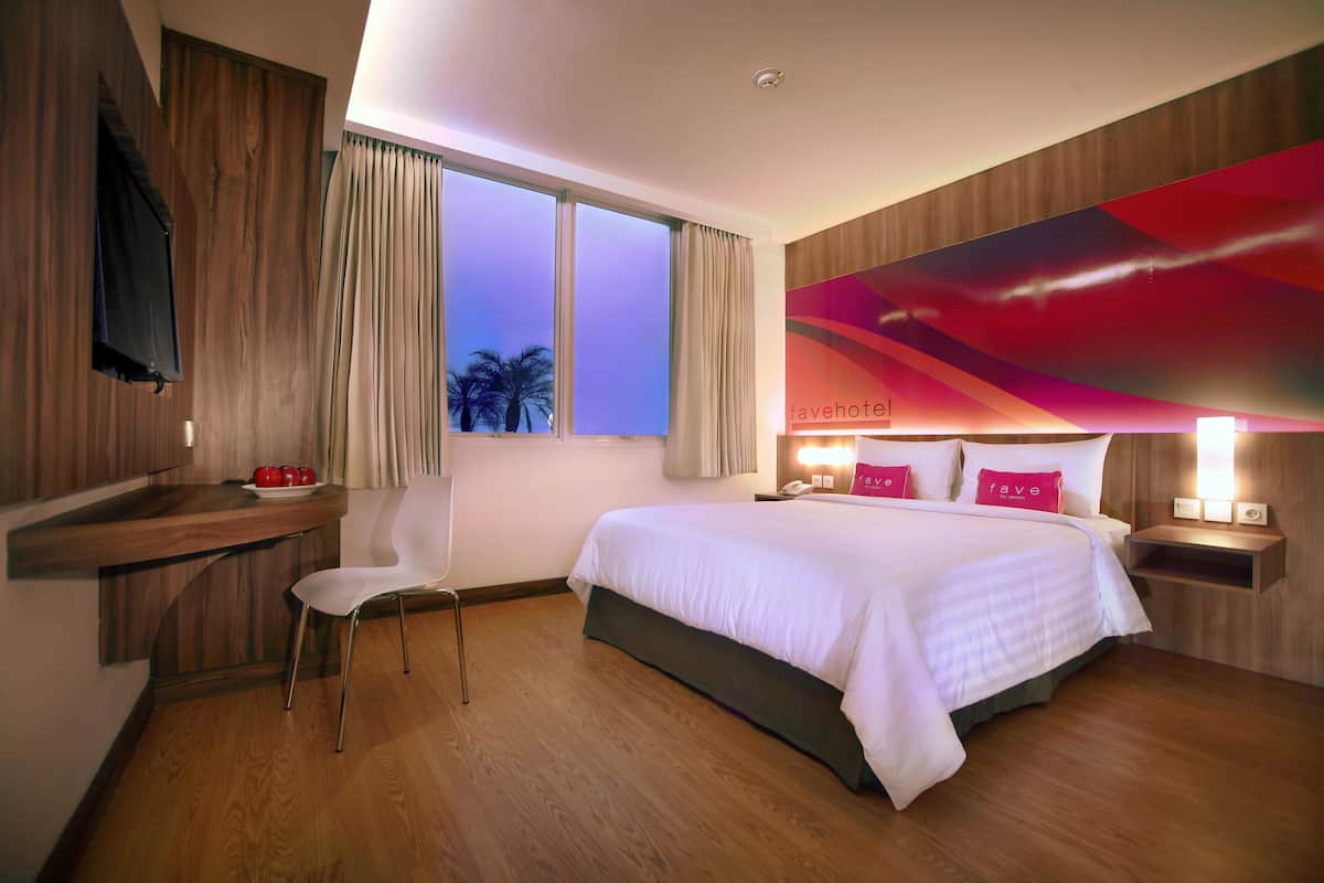 Hotelkamer met een bed, een bureau, een stoel, een nachtkastje en een raam met gordijnen.