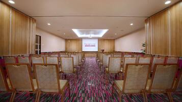 A conference room with a large screen displaying 'favehotel' at the front, rows of wicker chairs, and a patterned carpet.