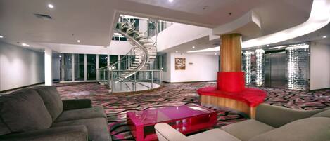 A spacious lobby with a spiral staircase, a red cylindrical column, and a patterned carpet.