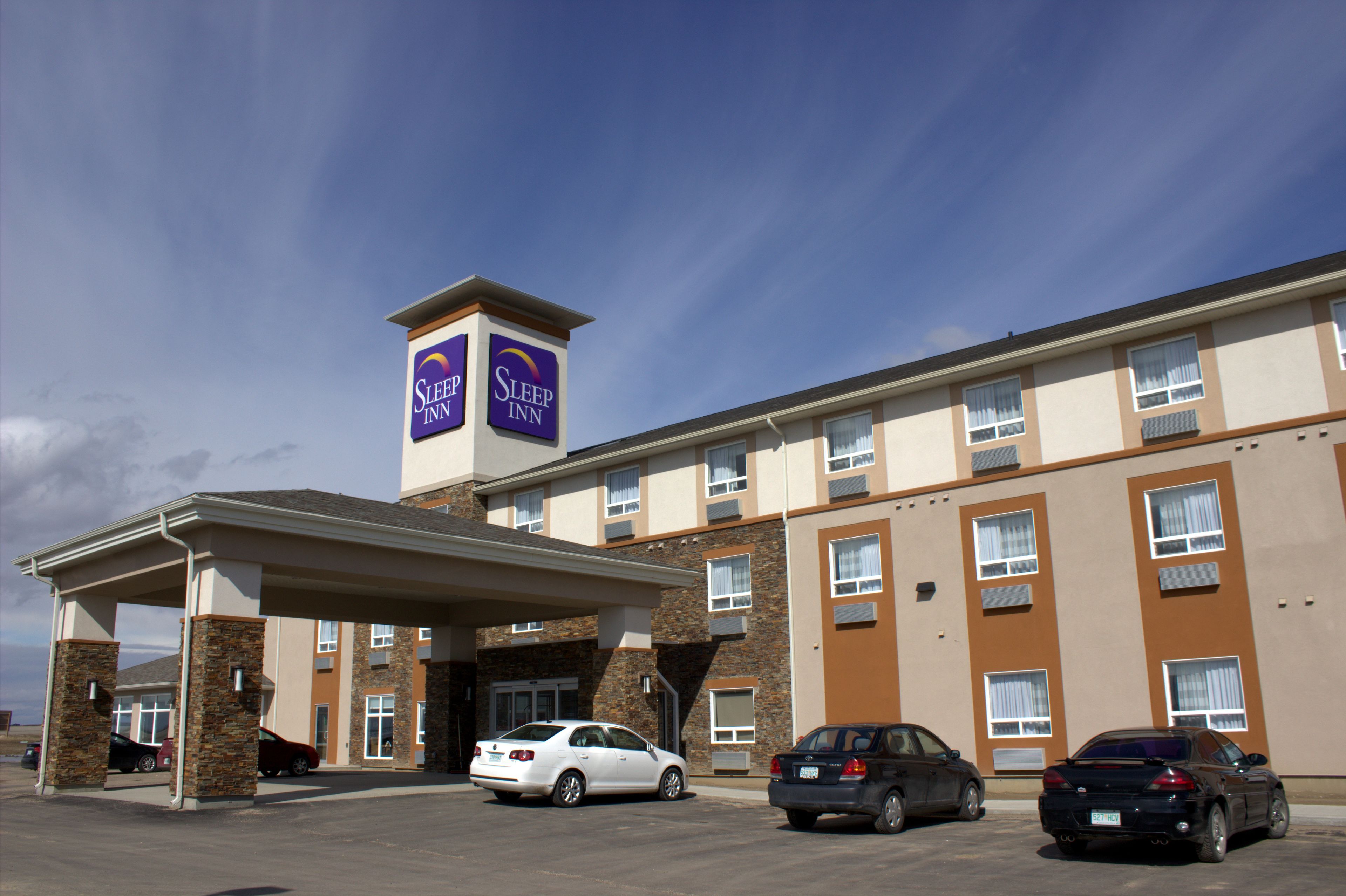Un hotel Sleep Inn con área de estacionamiento techada y varios coches estacionados al frente.