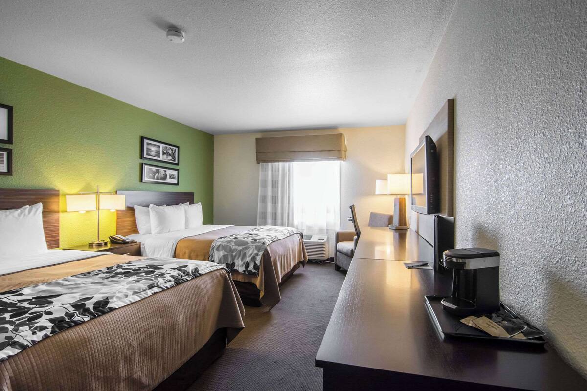 A hotel room with two beds, a desk with a coffee maker, a TV, and a window with curtains.