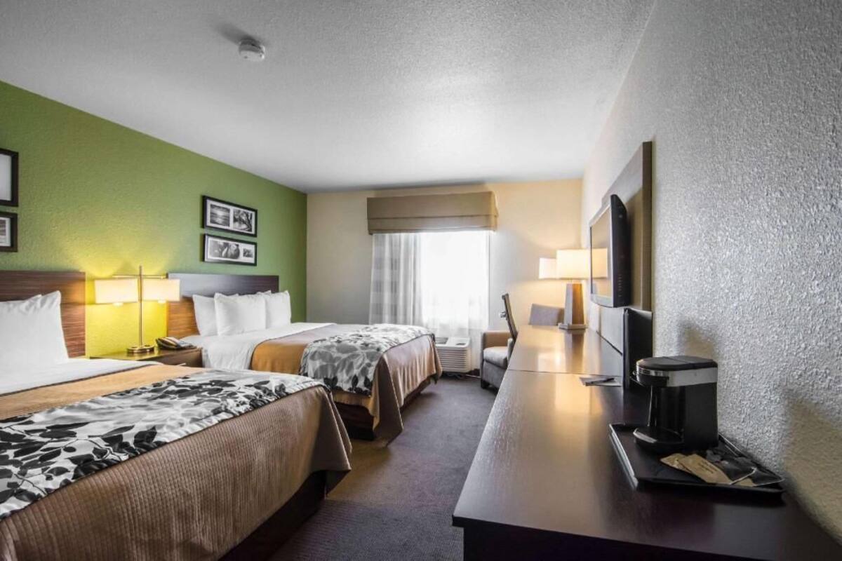 A hotel room with two beds, a desk with a coffee maker, a TV, and a window with curtains.