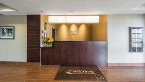Un área de recepción con un mostrador de madera oscura, un letrero de 'Sleep Inn' y un tapete de bienvenida.
