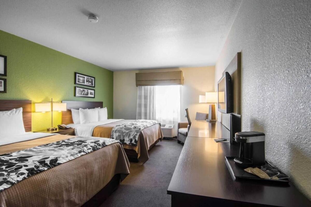 A hotel room with two beds, a desk with a coffee maker, a TV, and a window with curtains.