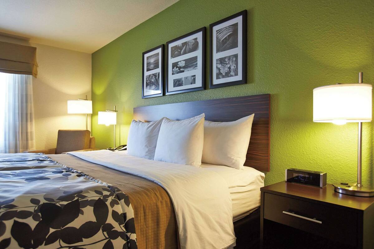 A hotel room with a bed, bedside lamps, a nightstand with a lamp, and three framed pictures on the wall.