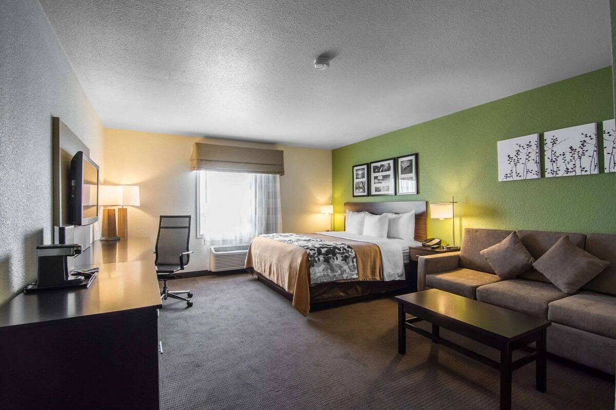 A hotel room with a bed, a desk with a TV, a chair, a sofa, and a coffee table.