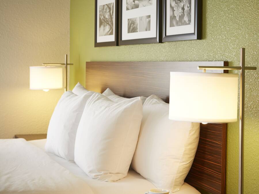Una camera d'albergo con un letto, cuscini, un comodino con una lampada e quadri appesi al muro.