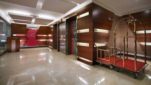 Un hall d’hôtel moderne avec un comptoir d’accueil, des ascenseurs et un chariot à bagages.