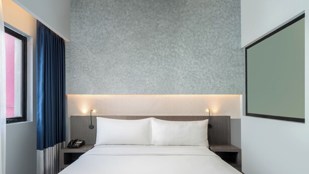 Une chambre d’hôtel avec un grand lit, des tables de chevet, un téléphone et un écran fixé au mur.
